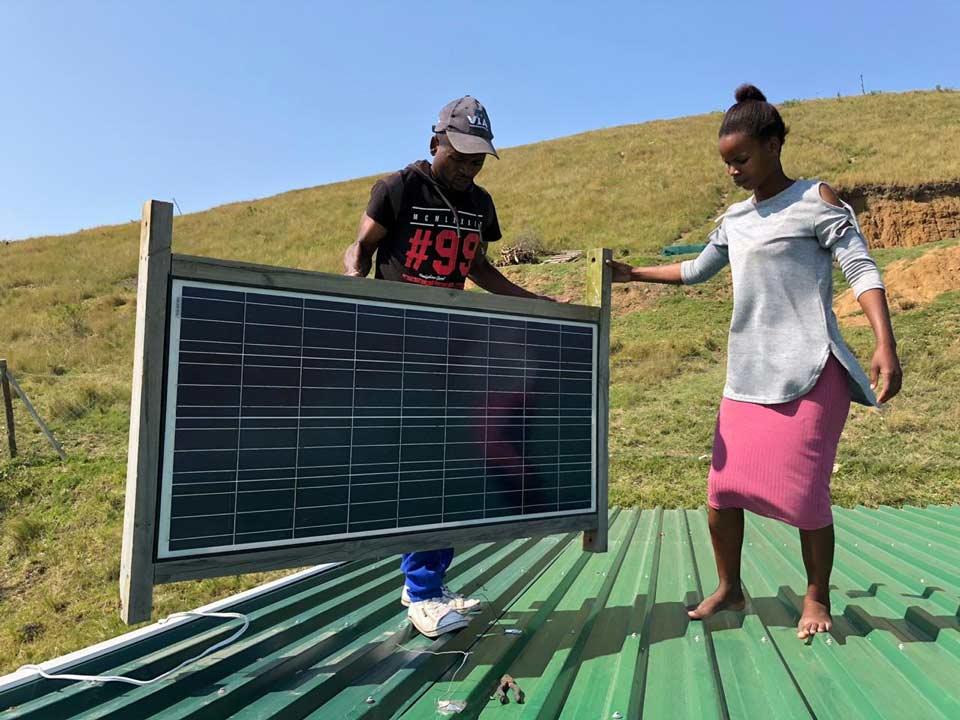 Image description: A man and a woman hold a solar panel on a roof