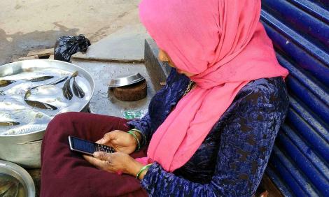 Image description: woman with mobile phone seated outside shop