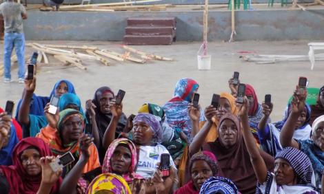 Image description: Photo of women holding up basic mobile phones