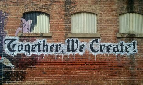 Graffiti saying "Together We Create" on a brick wall