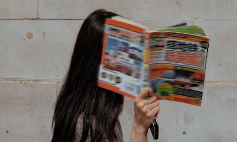 Image description: woman walking by, covering her face with Chinese magazine
