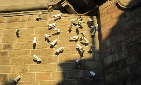 Image description: Numerous surveillance cameras on a wall 